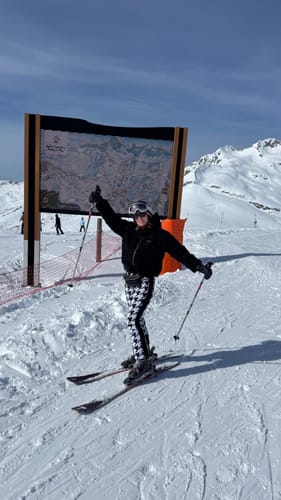 Customer posing on skis in the slim fit ski pants on a snowy mountain slope.