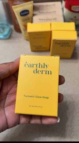 A customer holding the yellow box of Turmeric Fade & Glow Bar, with more boxes in the background.