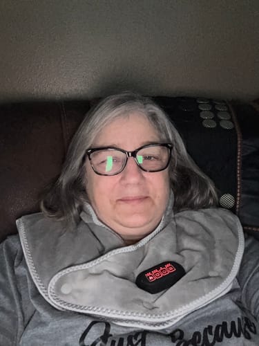 Reviewer sitting on a couch wearing the grey Callixe Thera Wrap, with the control panel lit up on their chest.