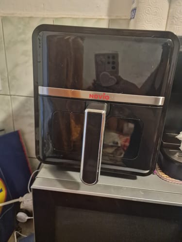 Clientul arată o friteuză neagră cu aer cald în care folosește hârtia de copt.