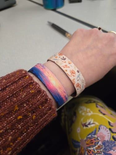 Customer wearing the One Day At A Time Bracelet with a vibrant sunset design, stacked with another floral bracelet on their wrist.
