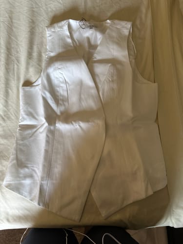 Una clienta muestra el VEST GIA blanco extendido sobre una superficie clara, destacando su diseño cruzado.