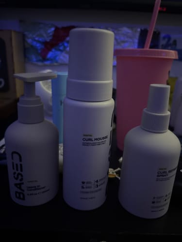 Customer's Based hair care products, including a conditioner, mousse, and spray, lined up on a dark surface.