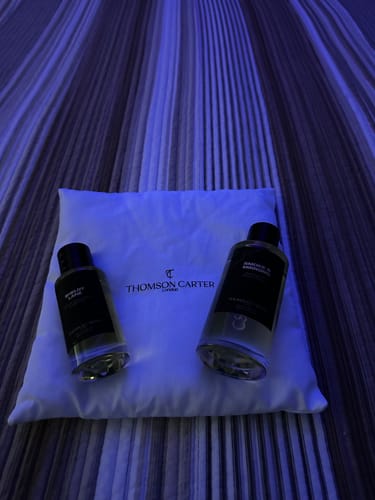 Reviewer's two bottles of Smoke & Mirrors Eau de Parfum displayed on a white pouch under cool blue light.