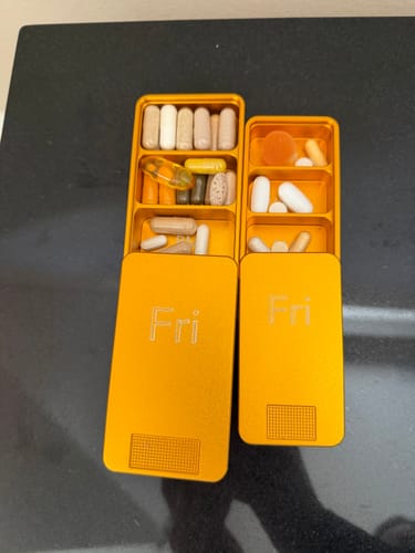 Customer's two orange metal pill cases, engraved with 'Fri' and open to show pills and vitamins inside.