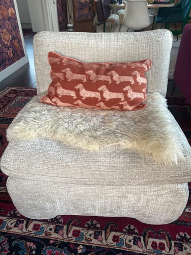 Klant's beige Pombo Fauteuil in een woonkamer, gestyled met een schapenvacht en een sierkussen.