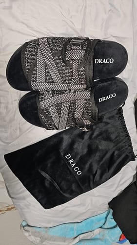 Customer's black Reflective Dracoslides with patterned straps laid out next to a black Draco drawstring bag on a bed.