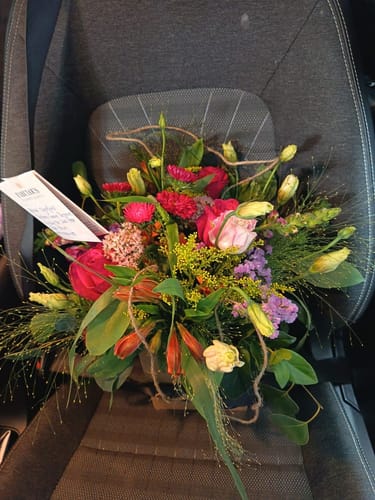 Customer's vibrant Summer Delight Posy Box, a fresh floral arrangement, sitting on a dark car seat.