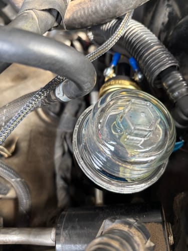 Close-up of a customer's SPE Motorsport ExoFilter installed, showing the clear lid among engine hoses and wires.