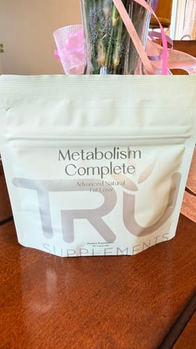 Customer's white pouch of Metabolism Complete supplements on a wooden table.