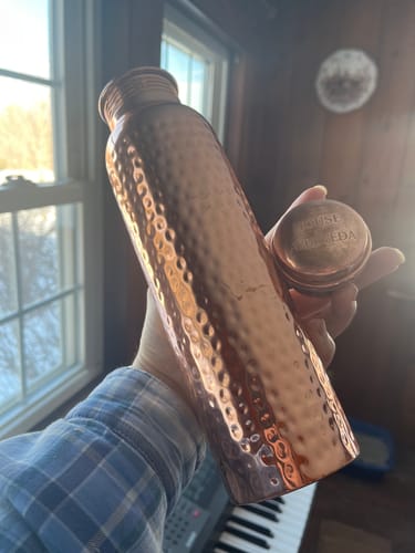 Customer holding the hand-hammered Pure Copper Water Bottle with its cap in their other hand.