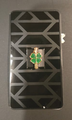 Customer's gold Lucky Charm with green fill shown on its black geometric packaging card.