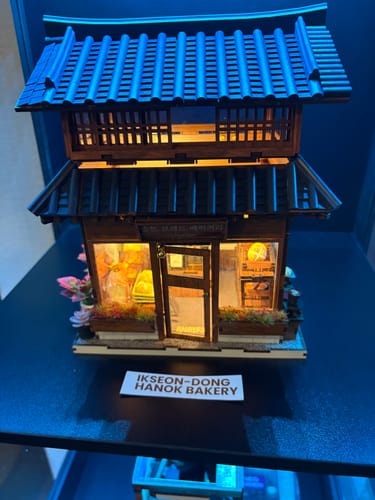 Customer's lit-up Ikseon-dong Hanok Bakery miniature on a shelf. The detailed wooden model shows a warm, glowing interior.