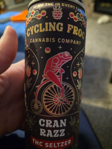 A customer holds the decorated can of Cran Razz THC Seltzer, showing the detailed frog illustration.