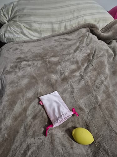 Customer's yellow Lem Clitoral Massager next to its small storage bag on a plush blanket.