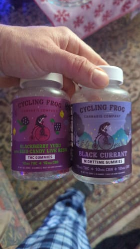 Customer's hand holding a bottle of Black Currant Nighttime Gummies next to another bottle of Cycling Frog gummies.