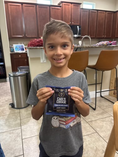 Customer's child smiles while holding a packaged Cael's Cookie — Chocolate Chip.
