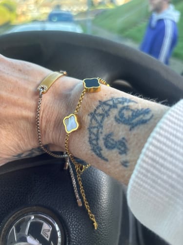 Customer's wrist wearing a gold-colored chain bracelet with black and white clover charms, next to a silver-colored bracelet.
