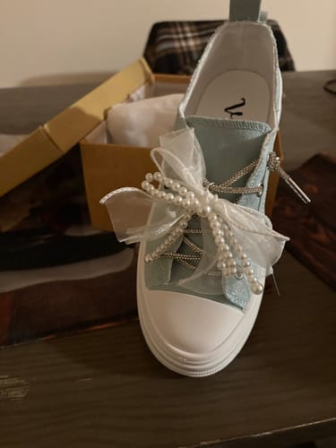 Customer's light blue Aman Pearls Sneaker with a sheer bow and pearls, resting on a table with its box open behind it.