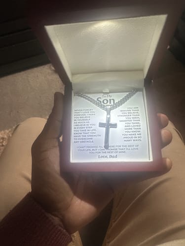 Reviewer holding the open mahogany-style gift box showing the Artisan Cross necklace illuminated by a built-in LED light.