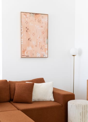 Customer's Love Is All Around art print hanging on a white wall above a rust-colored sofa.