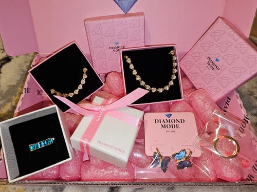 Ein Kunde zeigt das Drop Heart Armband und anderen Schmuck in einer rosa Markenverpackung.