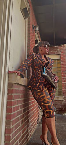 Customer posing in the Suiting Tortoise Capri Pants and matching blazer against a brick wall.