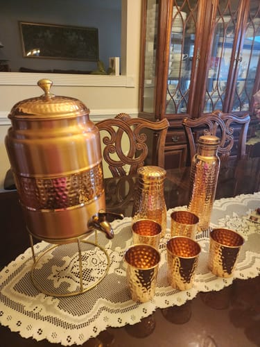 Customer's Copper Water Dispenser on its stand, shown with matching hammered cups and bottles on a table.