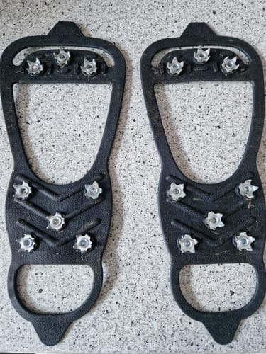Kunde zeigt die Unterseite eines Paars schwarzer Grip Spikes mit Metallstollen.