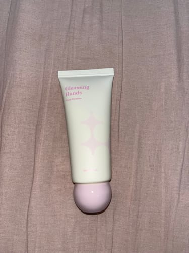 Customer's Gleaming Hands cream in Petal Paradise, showing the white tube with its round pink cap on a cloth background.