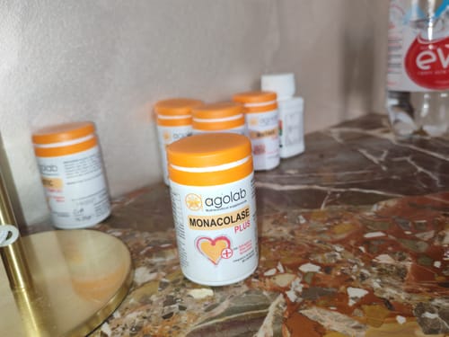 Una confezione di Monacolase PLUS del recensore in primo piano su un ripiano di marmo, con altre confezioni dietro.