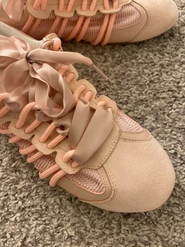 Close-up of a customer's single pink SHERYL sneaker, highlighting the large satin ribbon lace.