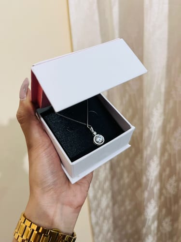 Customer's hand holding an open white box displaying the Silver Drizzle Drop Pendant on a black insert.