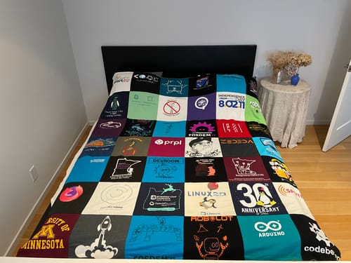 Customer's colorful Premium T Shirt Quilt made from various tech-themed t-shirts, spread neatly across a bed.