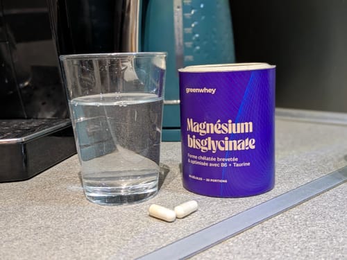 Avis du client : le pot de Magnésium Bisglycinate à côté d'un verre d'eau et de deux gélules sur un comptoir de cuisine.