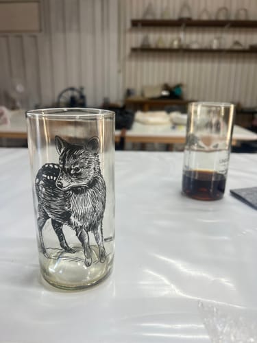 Cliente muestra un vaso transparente de la colección Fauna Chilena con una ilustración de una güiña sobre una mesa.