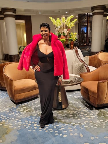 Reviewer celebrating in the black Hourglass Mesh Contrast Dress, styled with a bright pink coat.