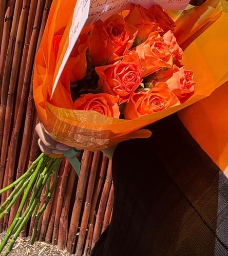 Customer holding their Harmony Flower Arrangement, a bouquet of bright orange roses.