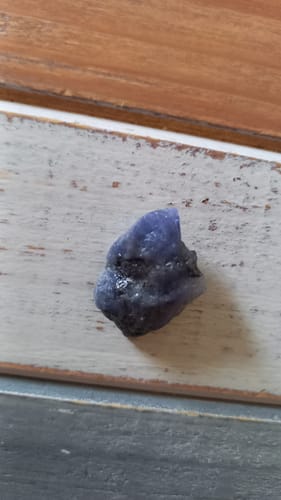 Photo d'un client montrant une petite tanzanite brute sur une surface en bois.