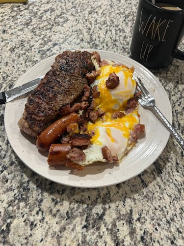 Customer's cooked USDA Choice steak served on a full plate with fried eggs and sausage.