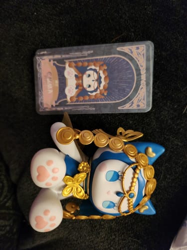 Customer's blue and white Emma Secret Forest figurine with gold details lying next to its matching character card.