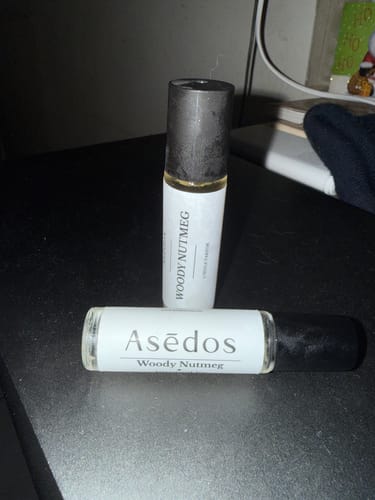 Customer's two glass roll-on bottles of Woody Nutmeg perfume oil on a dark tabletop.