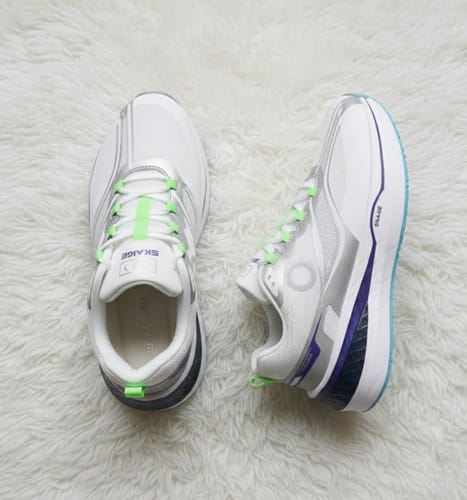 A reviewer's pair of white Cloud Walk shoes with green and purple accents, seen from the top and side on a fluffy rug.