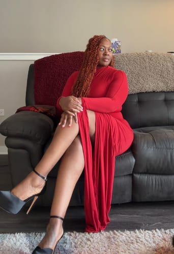 Reviewer sitting on a couch in the red Naked Draped Sleeve Maxi Dress, showcasing its high side slit.