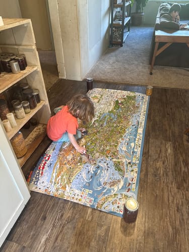 Customer's child playing with the large World's Greatest Search & Discover USA poster on a wooden floor.