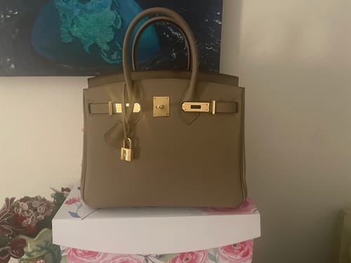Customer's taupe leather LALUVA Warkin Bag with gold hardware, shown on a decorative box.