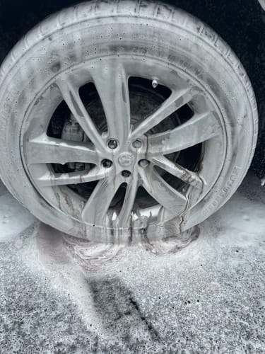 Customer's car wheel covered in white foam, with the Aurora Fallout Remover causing a purple reaction.