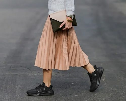Customer walking in black Cloud Walk shoes, paired with a long pleated skirt and sweater.