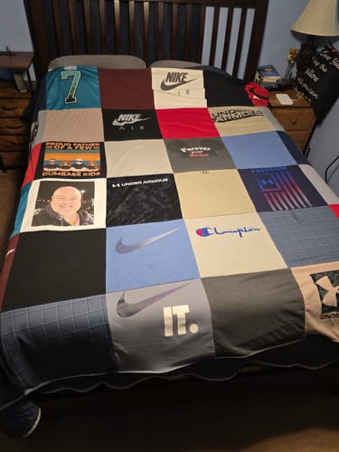 Customer's tribute t-shirt quilt spread on a bed, featuring squares with logos and a personal photo.