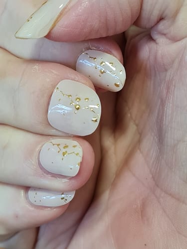 Close-up of a reviewer's hand with short nails wearing the Golden Veil gels with shiny gold flecks.